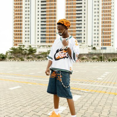 A stylish person in urban attire poses outdoors against city skyscrapers.