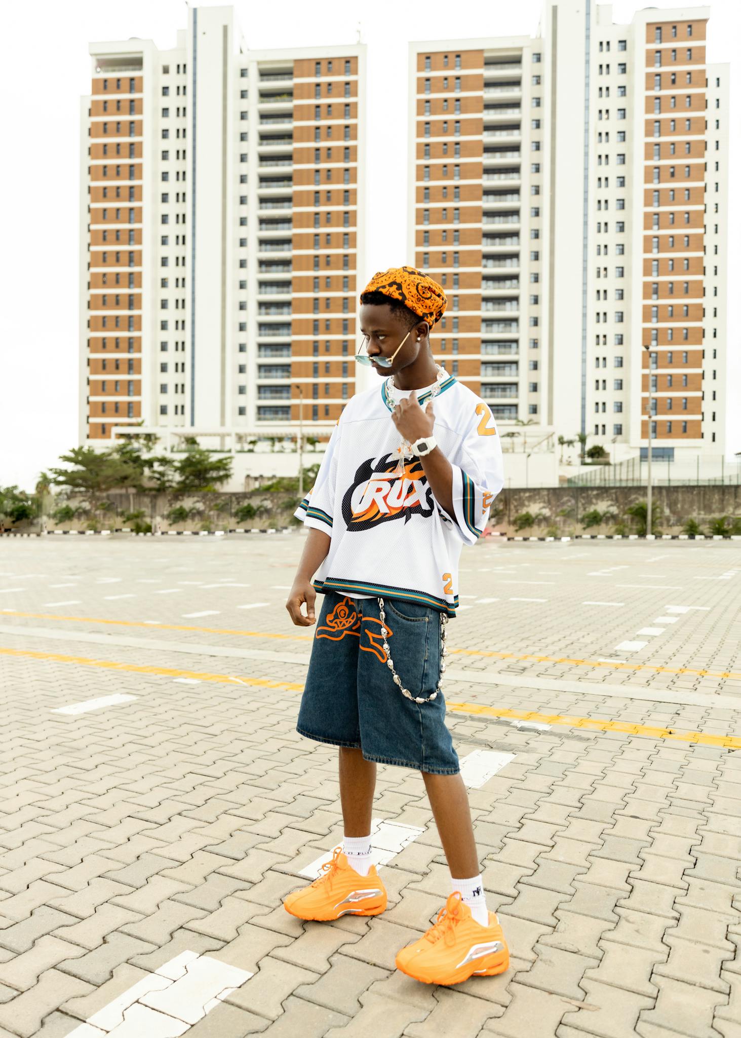 A stylish person in urban attire poses outdoors against city skyscrapers.