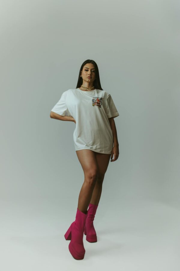 Fashion-forward woman poses confidently in bold pink boots and casual white t-shirt on a gray background.