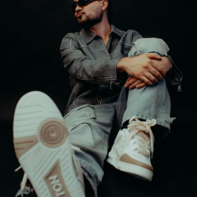 Model sitting in studio showcasing trendy designer sneakers and sunglasses with a bold style.