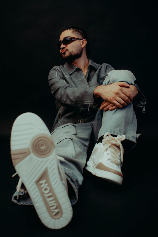 Model sitting in studio showcasing trendy designer sneakers and sunglasses with a bold style.