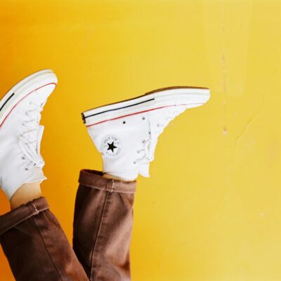 Upside down image of white sneakers against a vibrant yellow background, showcasing trendy footwear style.